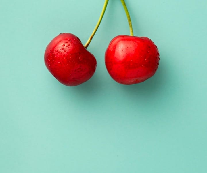 a pic of two cherries with a kinda greenish background color